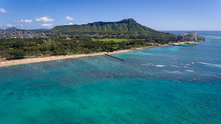 Turquoise sea with a sandy beach and green hill on the shore under a blue sky