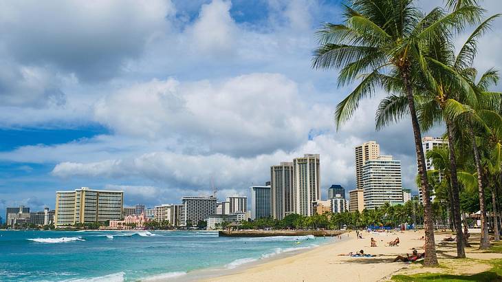 A beach with palm trees on the shore and buildings in the distance