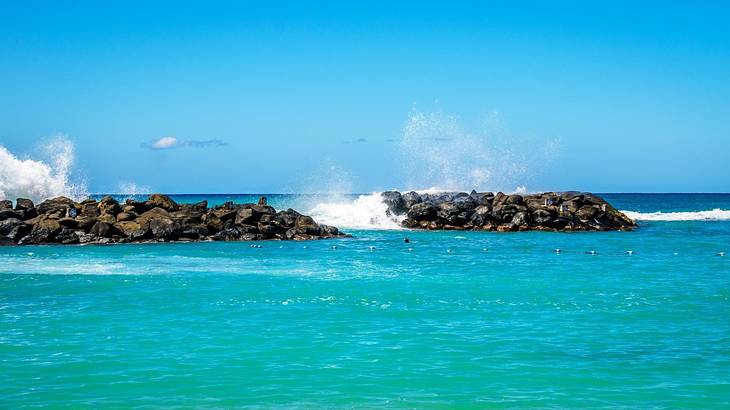 Bright blue ocean water and waves crashing onto rocks that are in the water