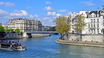 A river with a boat on it and trees and white Parisian buildings on the riverside