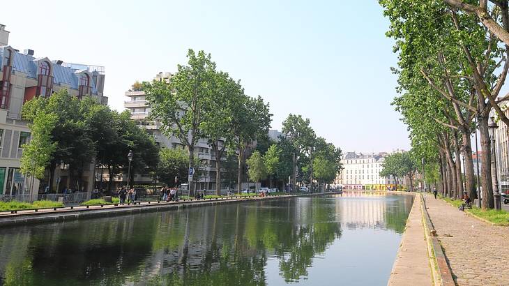 A canal with a path and trees on one side and buildings on the other side