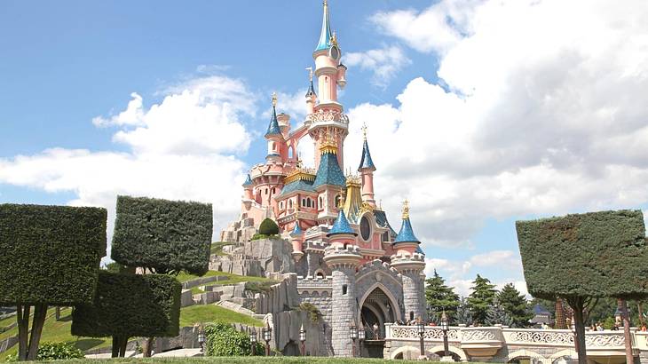 A pink Disney castle with trees in front of it under a blue sky with clouds