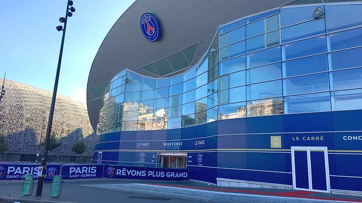 The entrance to a blue and glass sports arena with a Paris Saint-Germain logo