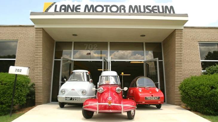 A museum with a "Lane Museum" sign and three vintage cars in front of it