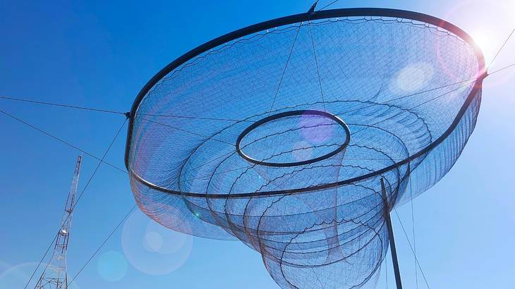 A tall sculpture with two metal rings and netting in the middle of a clear blue sky