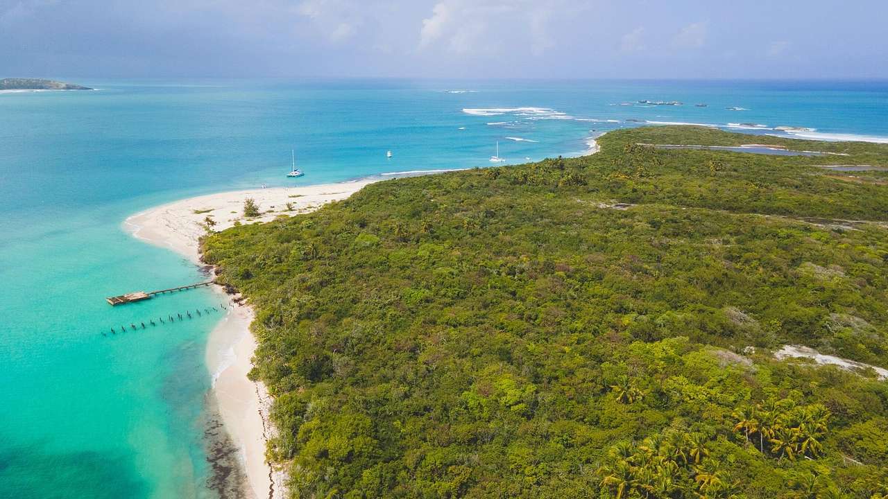 A greenery-covered island with turquoise water and white sand shores around it