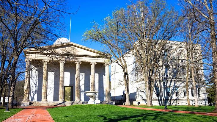 A neoclassical white building with deciduous trees in front of it under a blue sky