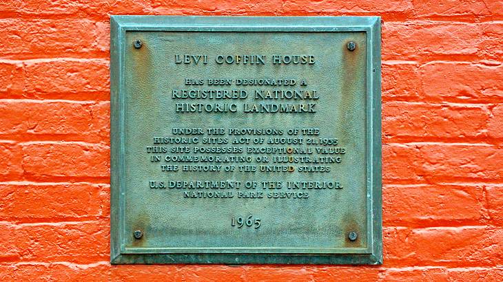 A red brick wall with a metal sign of "Levi Coffin House"