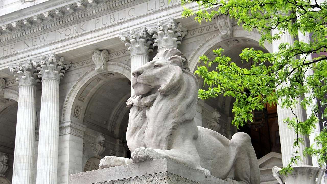 A stone lion statue sitting outside a stone New York Public Library building