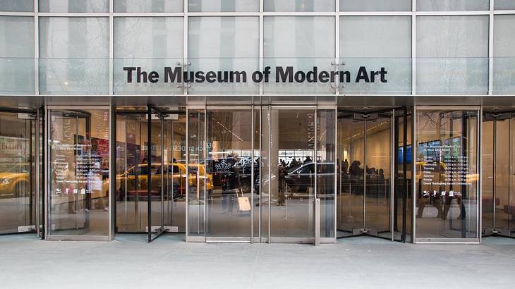 The entrance to a glass-front museum with a "The Museum of Modern Art" sign