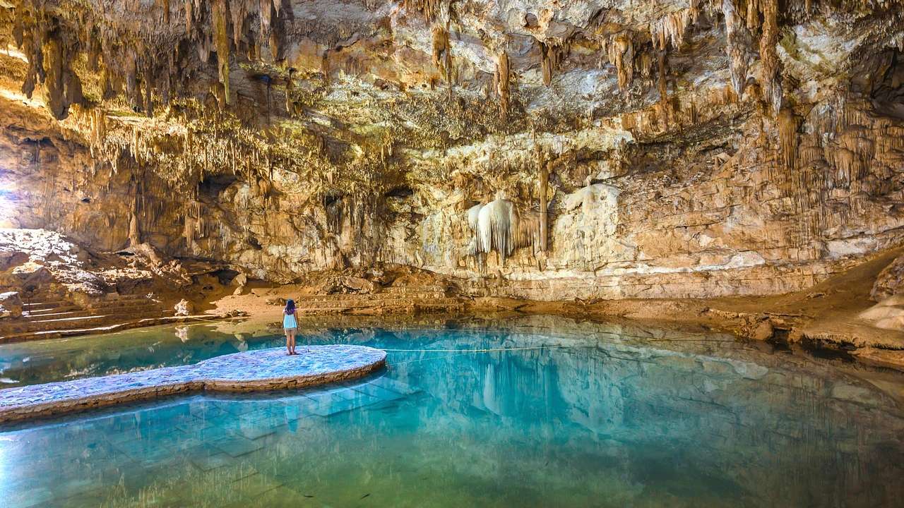 An underground pool with stalactites and a girl on a rock platform in the center