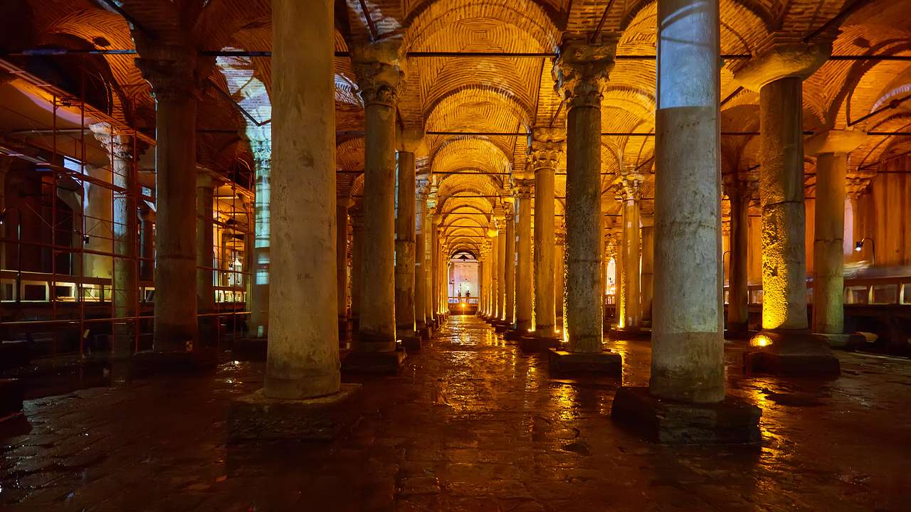 A dark room with yellow lighting and archways made from stone pillars