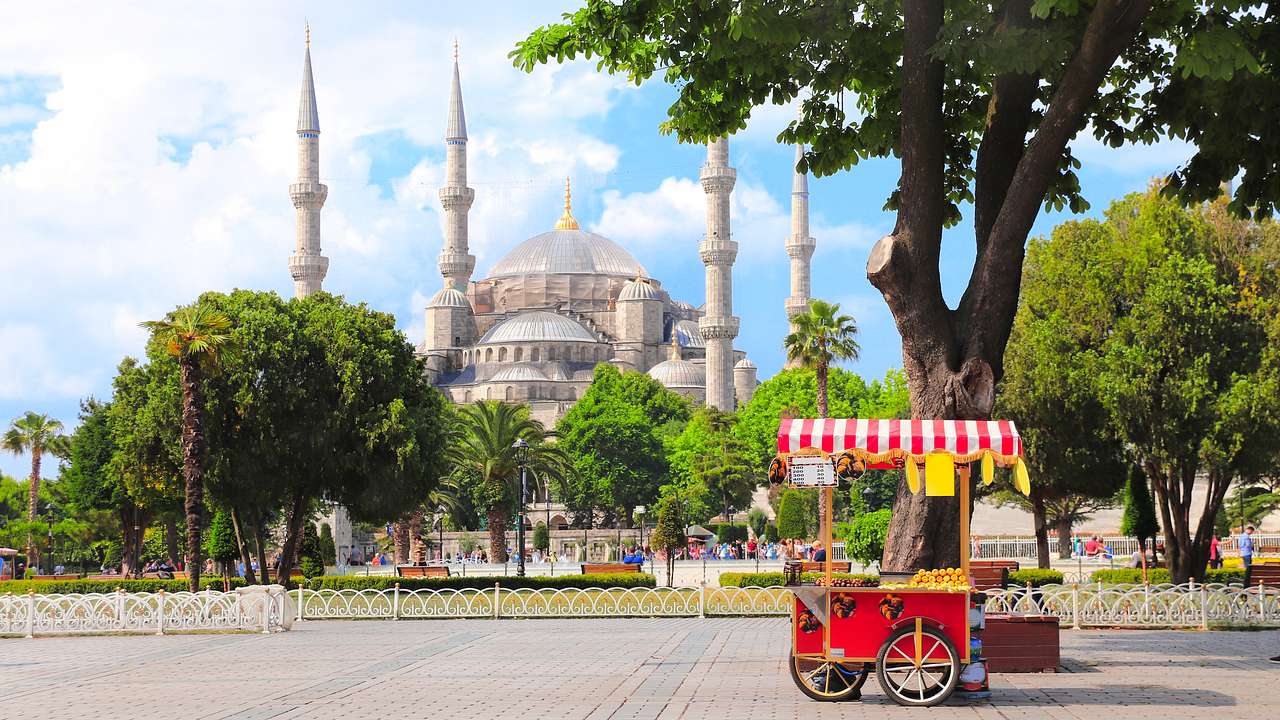 A red street cart against green trees and a mosque
