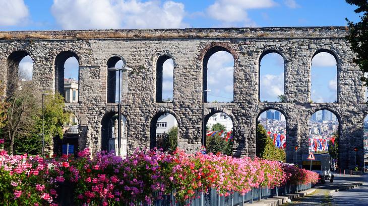 A stone structure with arches and pink and purple flowers in front of it