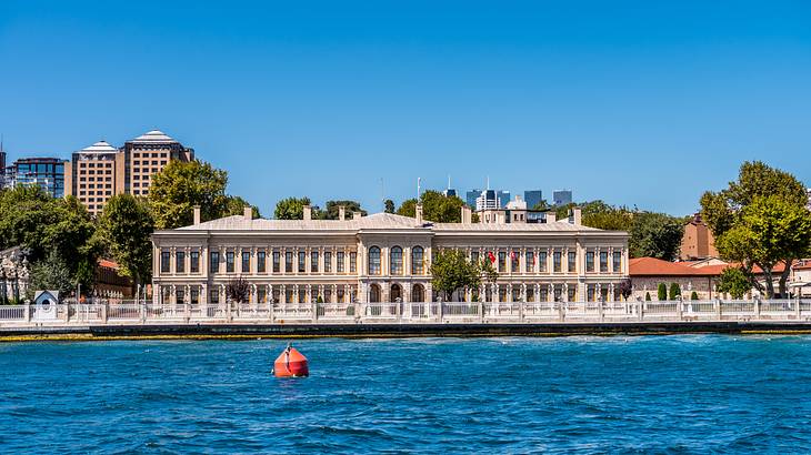 A wide stone building with many windows next to blue water on a clear day