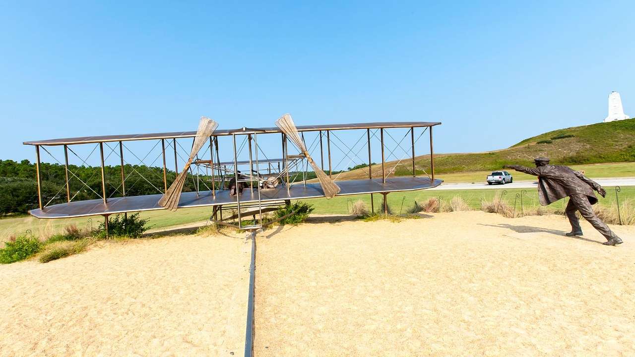 A replica of an old-fashioned plane and a statue of a man on sand