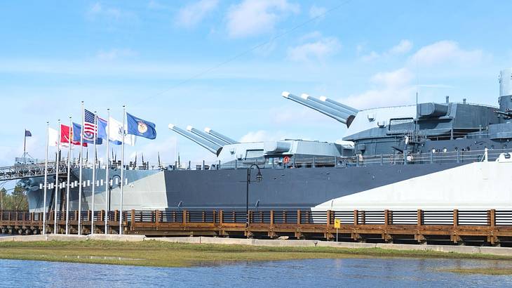 A military boat with flags, water, and grass in front of it