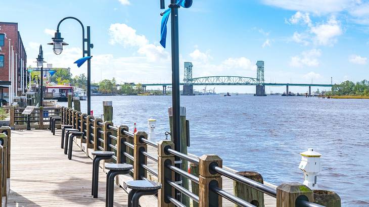 A riverwalk next to a river with a bridge in the distance