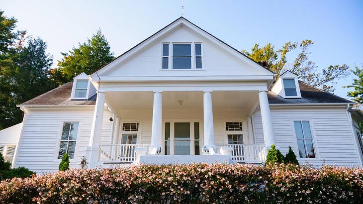 A white house with bushes and trees around it on a clear day