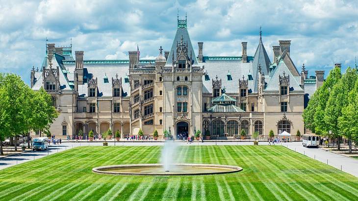 A large mansion house with green grass, trees, and a fountain in front of it