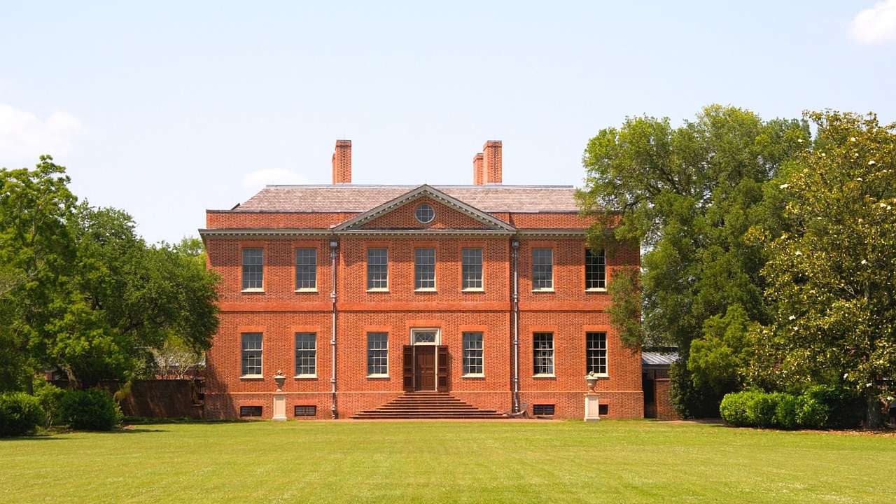 A red brick house with grass and trees surrounding it