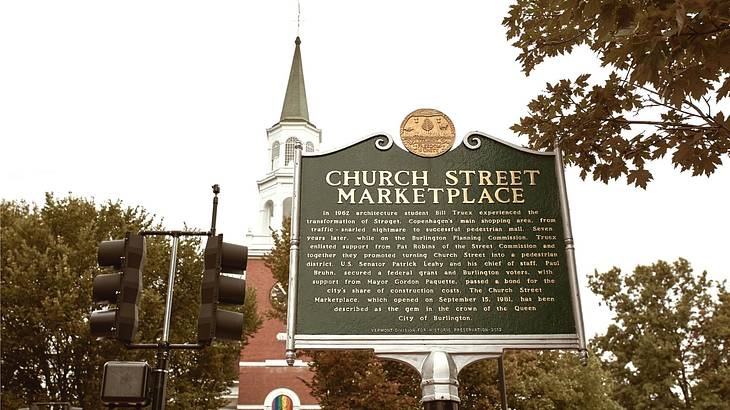 A sign that says "Church Street Marketplace" with a red brick church and trees behind