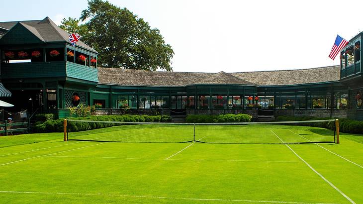 A tennis court with a green lawn and a long building behind it on a clear day
