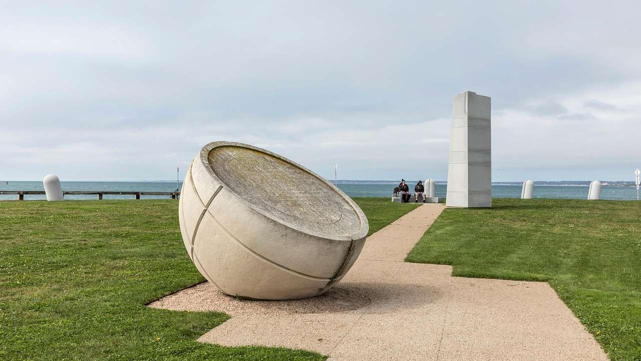 A half globe stone structure sitting on a path next to grass on a cloudy day