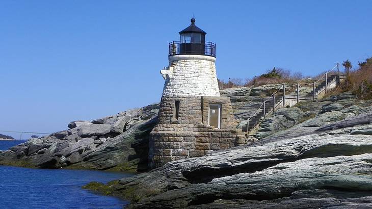 A small lighthouse surrounded by rocks and water under a clear blue sky