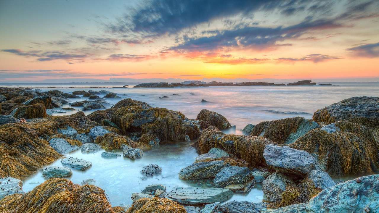 A sunrise over rocks surrounded by water with a light fog over it