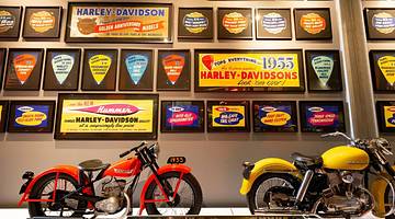 Two motorcycles and a wall of Harley-Davidson Museum plaques in a museum