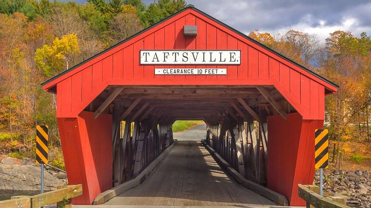 A red wooden covered bridge with a sign that says "Taftsville, clearance 10 feet" A red wooden covered bridge with a sign that says "Taftsville, clearance 10 feet"
