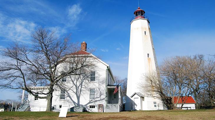 A white lighthouse with a red top next to a white house with bare trees in front