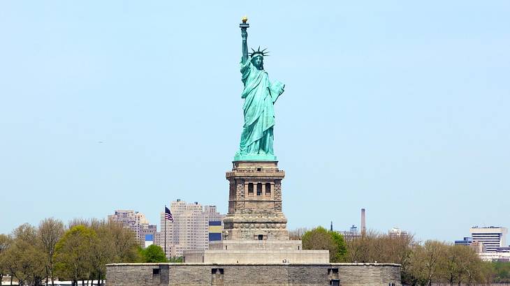 The Statue of Liberty with trees on either side under a clear blue sky