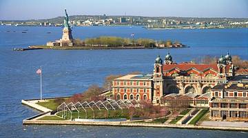 A red brick building on an island with the Statue of Liberty behind it