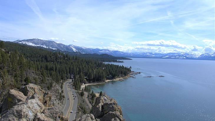 Aerial view of a road adjacent to Lake Tahoe, with a mountain range in the back
