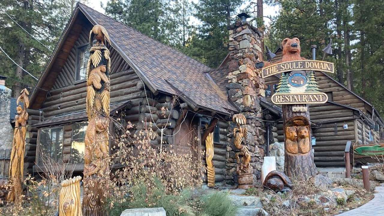 View of a restaurant with totem poles and evergreens around, that looks like a cabin