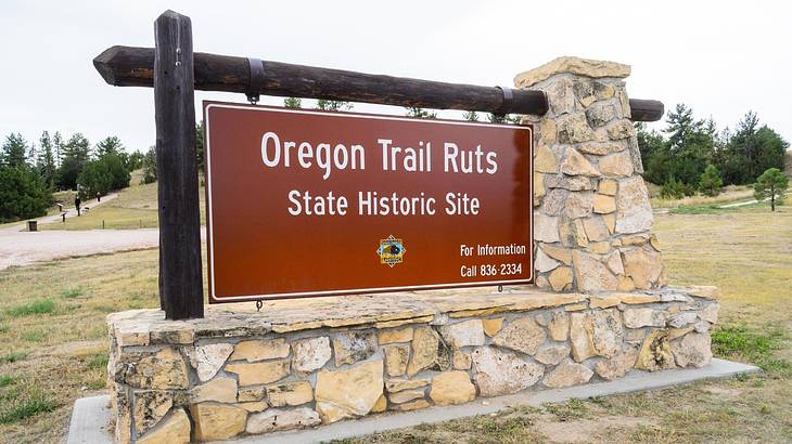 A brown sign that says "Oregon Trail Ruts State Historic Site" with greenery behind