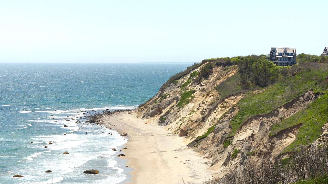 Cliffs with grass and a house on them and ocean water and a sandy shore below them