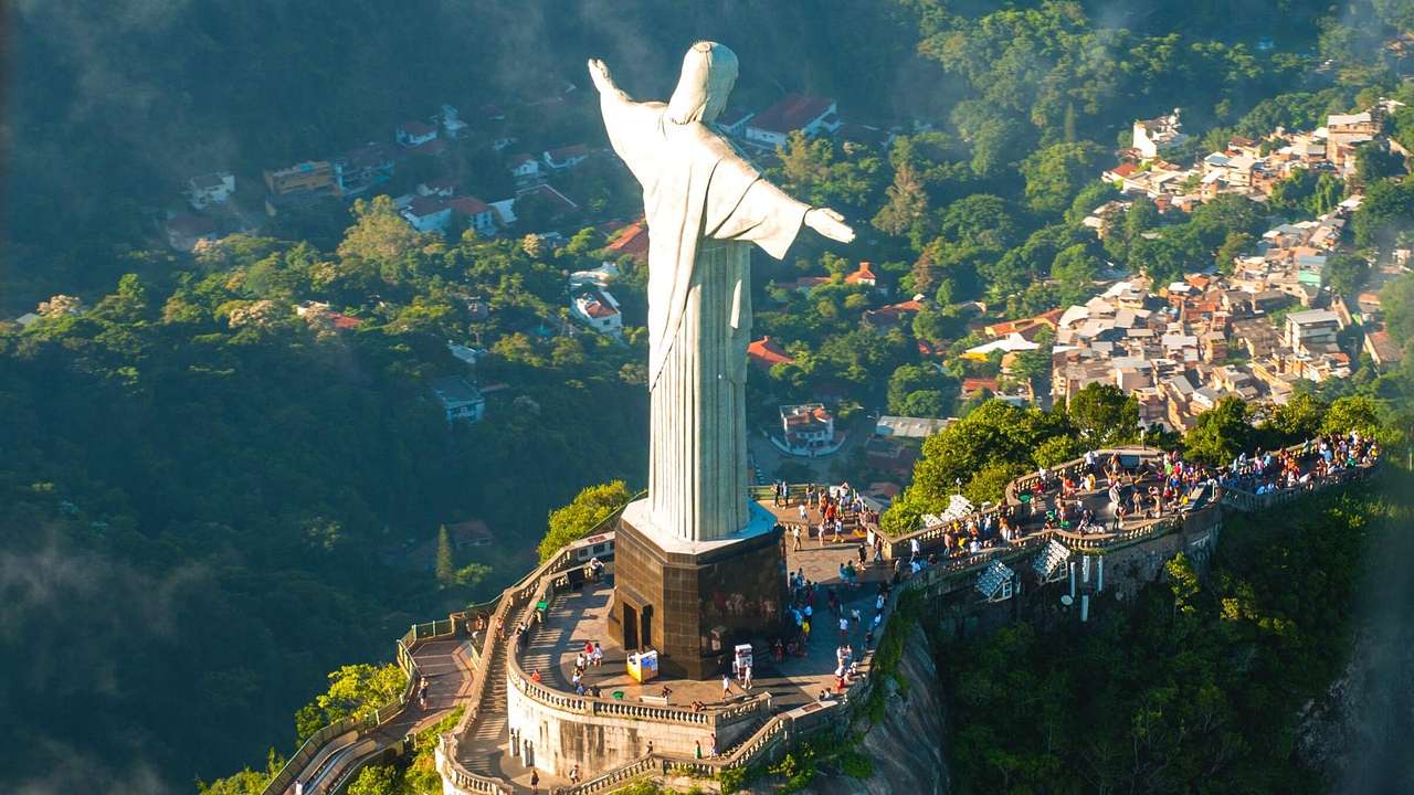 An aerial view of a tall statue of Jesus on top of a mountain with tourists around it
