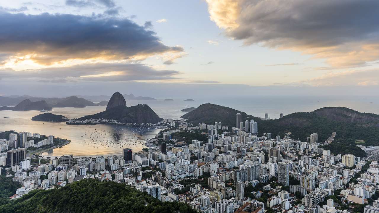 A panoramic view of a city with buildings surrounded by hills and water at sunrise