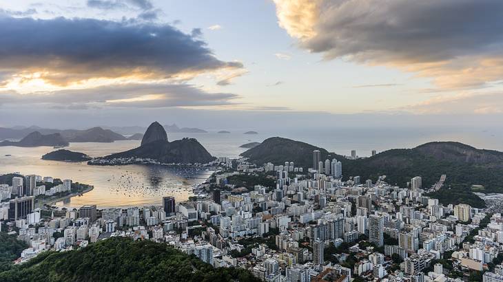 A panoramic view of a city with buildings surrounded by hills and water at sunrise