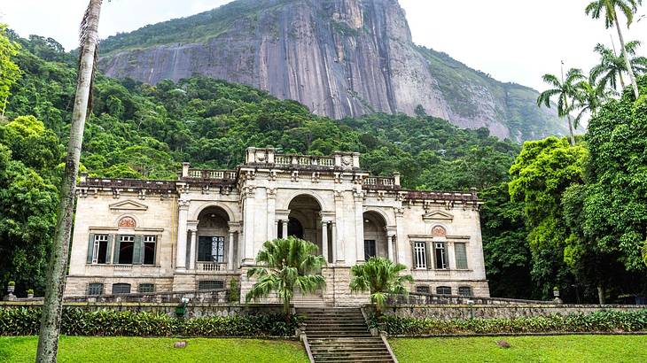 A staircase leading to an ancient stone mansion surrounded by trees and green grass