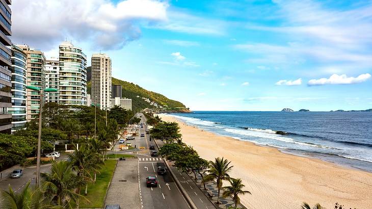 High-rise buildings next to a road overlooking a white sand beach and the ocean