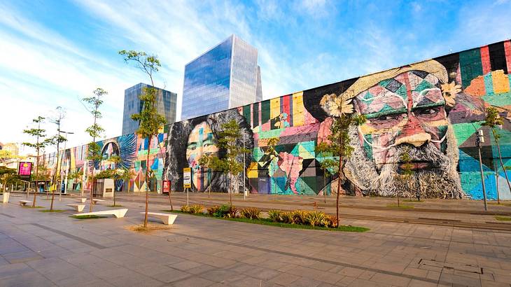 A long wall covered with a colourful street art mural and a street and trees in front