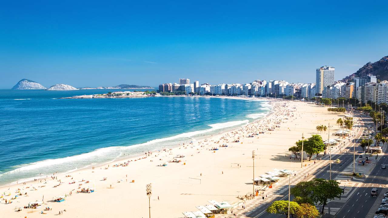 Tall white buildings along a white sand beach with a blue seashore to the side