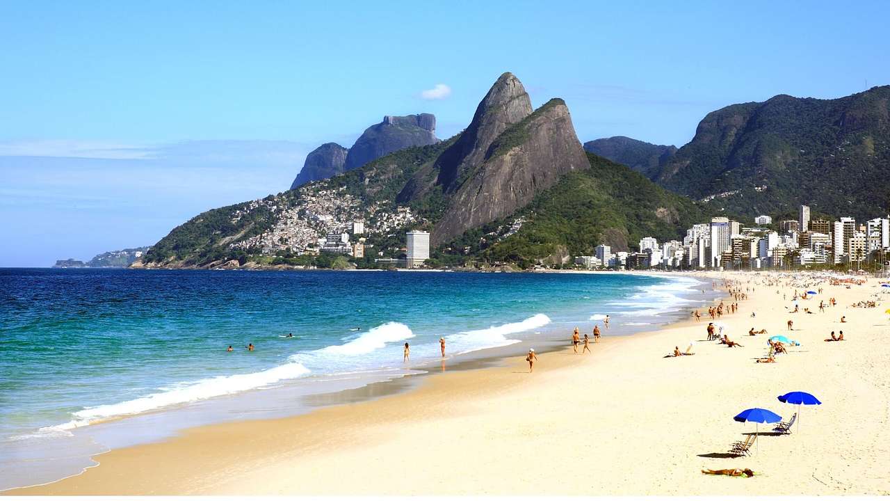 A white sand beach with buildings and greenery-covered mountains behind it