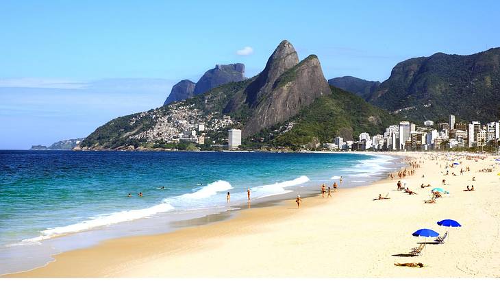 A white sand beach with buildings and greenery-covered mountains behind it