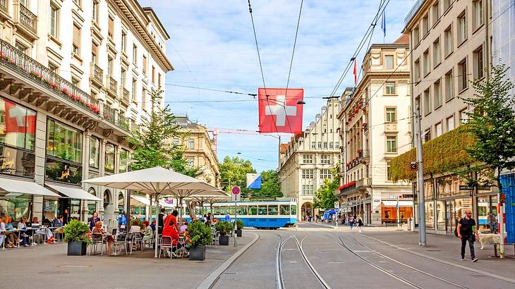 A tram track on a bustling road with shops and outdoor seating around it