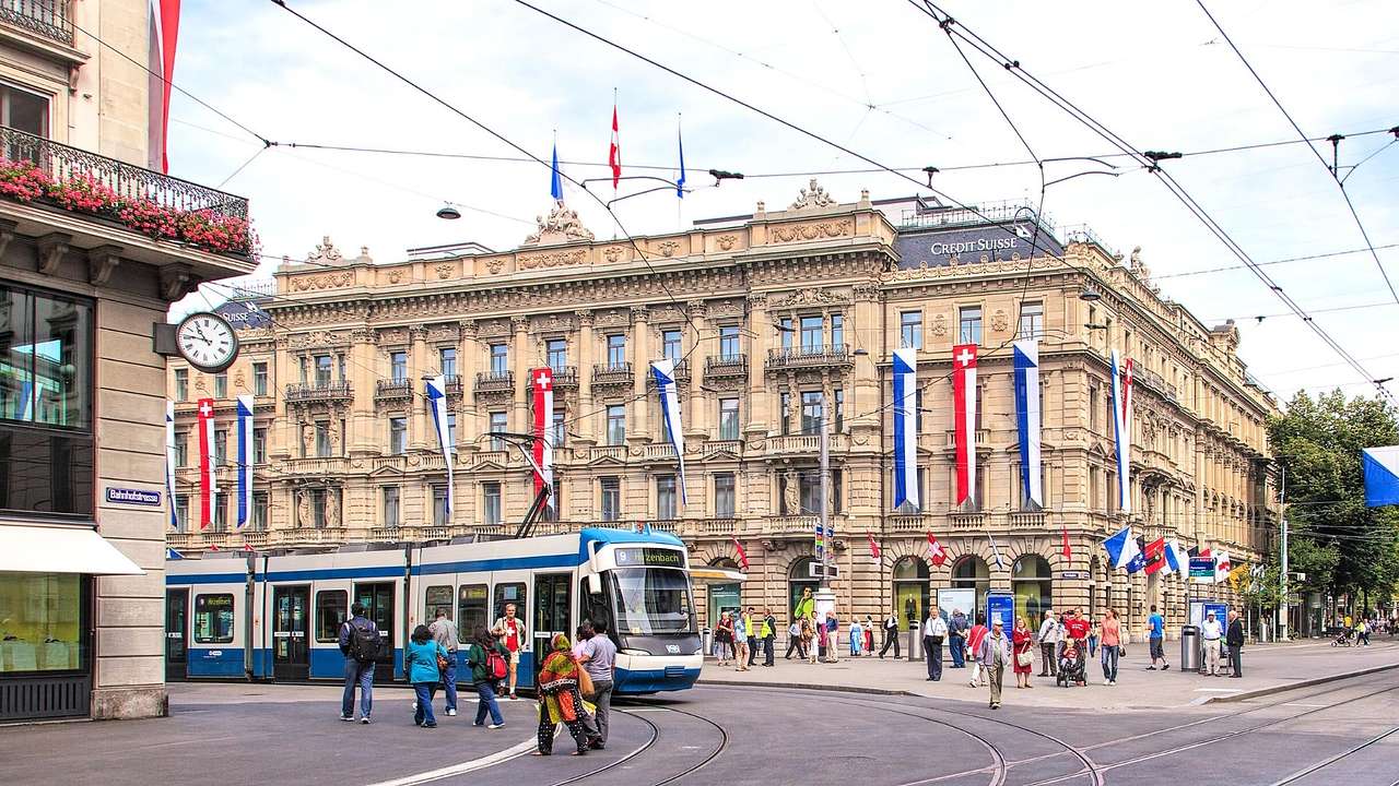 A blue tram on a street with buildings and people around it
